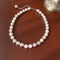 Dettaglio di perle bianche e sfere d'argento satinato su superficie marrone scuro - Collana Con Perle Argentate