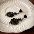 Détail macro de boucles d'oreilles cœur noir gothique avec strass sur un plat en céramique - Cœur en Strass Noir (Tige en Argent)