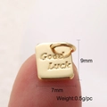 Makroansicht des goldenen 'Good Luck' Anhängers auf einer Fingerspitze zur Größendarstellung - Mini-Glücksanhänger
