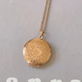 Macro detail of golden round locket necklace featuring embossed floral pattern and hinge - Rose Gold