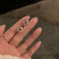 Boucles d'oreilles nœud torsadé argentées présentées sur doigt pour le détail - Boucle d'oreille / Argenté