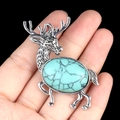 Antique silver elk brooch with oval turquoise stone held in hand for scale - Synthetic Turquoise