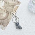 Close-up of grey flocked cat keychain with silver metal lobster clasp and ring on a desk - Lying Style Gray Cat