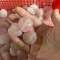 Hand holding pink rose quartz heart stones with gold Love engraving details - Love