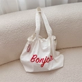 Dettaglio della borsa a secchiello in tela bianca con stampa Bonjour rossa su un divano - Bianco