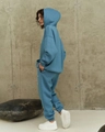 Side view of blue hooded sweatshirt and high-waist joggers set on industrial background - Teal