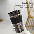 Smoky grey glass tumbler with black silicone sleeve, lid, and straw in hand - Smoky Grey + Black Lid + Clear Glass Straw + Black Silicone Sleeve