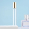 Clear glass roller bottle with golden cap on white stand against light blue background - 10ml Gold