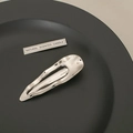 Detalle de pinza para el pelo ondulada de metal plateado en un plato negro - Gota de agua
