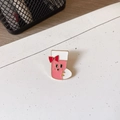 Detailed close-up of a pink cartoon Christmas stocking enamel brooch with a red bow accent - Socks