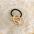 Close-up of a high-elastic black hair tie with a polished gold-finish knot metal detail - Gold Knot