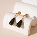 Primer plano de pendientes de gota oscuros con perlas de resina blanca en tachuelas doradas - Pin de Plata - Gota de Agua Negra Colgante