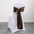 Brown satin chair sash tied in a large bow on a white spandex chair cover for weddings - Coffee
