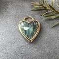 Detail of heart-shaped labradorite pendant with gold edging on a textured grey surface - Labradorite