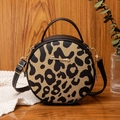 Chic leopard print round crossbody bag with metal handle on a stylish wooden background - Black