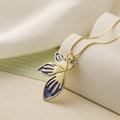 Minimalist gold necklace featuring a blue enamel leaf pendant on a white pedestal - Purple
