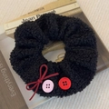 Detail of plush black scrunchie with red bow and pink buttons on textured fabric - Black