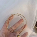Detailed close-up of large polished gold hoop earrings held against soft white fabric background - 7cm / Minimalist Hoop / Gold