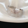 Detail van een zilveren meerlaagse armband met golvende textuur op witte zijden stof - Armmanchet / Zilver