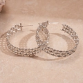 Detailed close-up of silver braided hoop earrings on a textured neutral surface - Silver