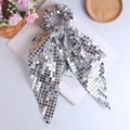 Close-up of silver sequin scrunchie with long bow ribbon on an open book surface - Silver