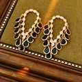 Vue détaillée des boucles d'oreilles dorées avec pierres noires sur velours vert - Or-Noir