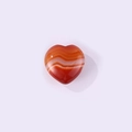 Polished heart-shaped natural agate stone with red and orange stripes on purple background - Banded Agate