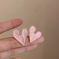 Dettaglio di orecchini a cuore rosa irregolari con finitura metallica ruvida sulla mano - Cuore Pieghettato Rosa