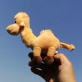 Detailed view of a tan camel plush keychain held against a bright blue sky background - Camel-Light Yellow / 12cm