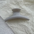 Detail of a minimalist grey PC hair claw clip on a textured beige and white background - Grey/White