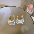 Detail of gold metal and clear acrylic U-shaped geometric earrings on a mirror surface - U-Shaped Geometric Patchwork Style / Hoop Buckle Style / Gold