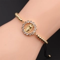 Detail eines Goldperlenarmbands mit Jungfrau Maria Medaillon und Zirkonia-Akzenten - Goldene Kupferperlen + Schwarzes geflochtenes Seil