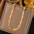 Detalle de un collar de cadena plana trenzada dorada sobre un joyero de color beige - H308 Collar De Doble Vuelta Dorado
