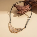 Detail of golden leaf pendant with brushed texture on black cord necklace set on wood - Gold