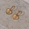 Close-up of golden heart earrings with angel relief and textured rope edges on stone - Heart Angel Earrings