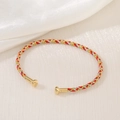 Macro shot of tricolor braided bracelet with red gold silver threads and metal clasp - Red Gold Silver