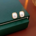 Close-up of square pearl earrings with gold frames on a dark green jewelry box backdrop - Gold Square (925 Silver Pin)