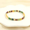 Macro detail of colorful Tila bead tile bracelet with gold accents on white tray - Multicolor H-Red Yellow Green Black Brown Gold