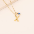 Détail macro du pendentif lettre X doré et de l'œil bleu sur une chaîne épurée - Lettre X