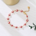 Close-up of golden evil eye bracelet with colorful enamel beads on a white textured cloth - Red Eyes Gold