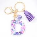 Macro detail of resin letter D keychain with colorful crushed stones and purple tassel - Letter D
