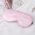 Pink satin silk sleep mask with eyelash print and elastic strap on plush rug - Pink