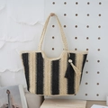 Schwarz-beige gestreifte Strohtasche mit Perlenquaste hängend an einer weißen Lochwand - Schwarz und Beige gestreift / Beige