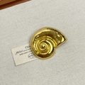 Detailed close-up of a golden snail-shaped minimalist brooch on a textured beige fabric - 27 Gold Conch (Z-4111)