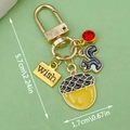Golden squirrel keychain with yellow acorn and red gemstone charm on green background - Pinecone Squirrel