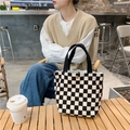 Detail of checkered canvas tote bag with black handles and gold buckle in a cafe setting - Black Check