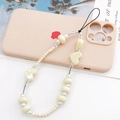 Beaded heart phone strap with beige pearls and charms on white surface with pink case - Beige