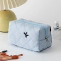 Detail of light blue quilted lipstick bag with embroidery in a cosmetic lifestyle setting - Light Blue