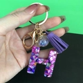Detail of purple resin letter H keychain with gold ring, tassel, and star glass ball - Letter H