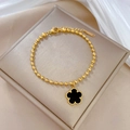 Détail du bracelet en perles dorées avec trèfle noir sur fond de soie blanche - Acier titane / Doré